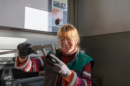 机床摄影照片_一名妇女在现代化金属生产和加工工厂工作，准备和测量用于数控机床加工的材料
