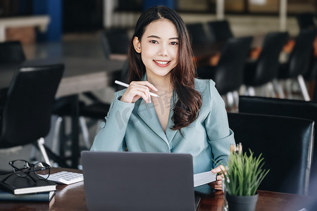 亚洲女企业家或女商人在阅读一本制定金融和投资策略的书并在木桌上操作平板电脑时露出微笑。
