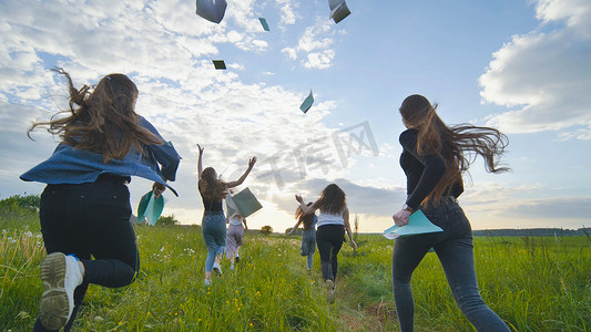 扔摄影照片_日落时分，快乐的学生放学后奔跑着扔笔记本。