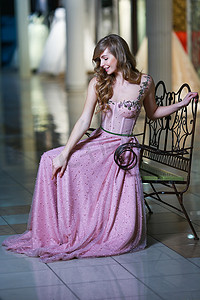 身穿粉色晚礼服的金发美女坐在金属长凳上