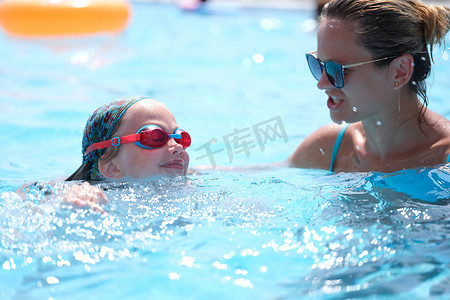 游泳培训摄影照片_女教练在泳池里教小女孩游泳