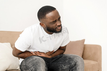 腹痛的黑人坐在家里的沙发上，胃部痉挛。