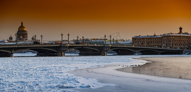 日落时圣彼得堡的冬季全景、艾萨克大教堂和布拉戈维申斯基桥的背景、冰冻涅瓦河上的蒸汽、橙色的天空