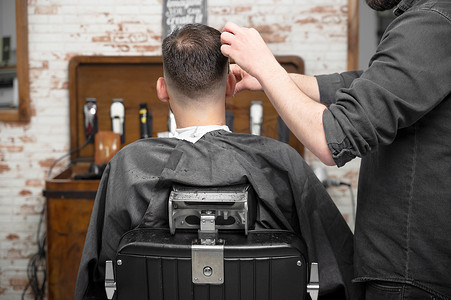 剪头发摄影照片_理发师用剪刀给一个英俊的年轻人剪头发。