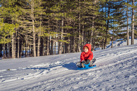 趣味摄影照片_快乐积极的小男孩享受雪橇和寒冷的户外天气，冬季趣味活动概念