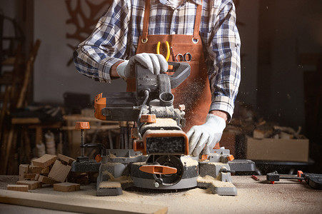 木匠正在木工车间用电动圆锯机锯切木板。