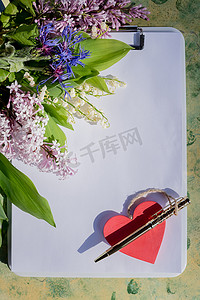 红色一张摄影照片_关于爱情的模拟信。红色木心躺在空白的白纸上，木桌上摆着春天的花朵，还有一张情人节贺卡，上面有文字的地方。