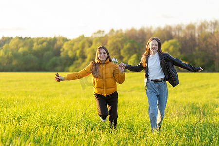 妈妈和女儿穿着休闲装在美丽的春天日落时在田野里奔跑。