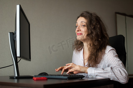 身着白衬衫和卷发的年轻女办公室经理坐在桌旁，用键盘打字，日常工作，自由职业者
