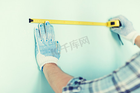 戴手套的男性用胶带测量墙壁的特写