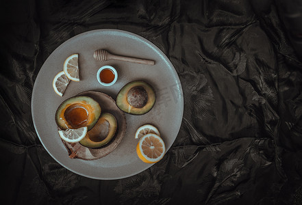 牛油果装饰背景摄影照片_新鲜有机牛油果切成两半，柠檬切片，蜂蜜用木棒蜂蜜勺。