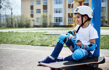 黄色建筑背景下，可爱的小男孩放松地坐在滑板上