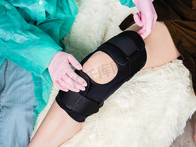 黑色膝盖摄影照片_一位家庭医生将黑色支架放在病人膝盖上的特写