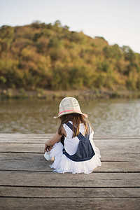 小女孩独自坐在河边的木桥上