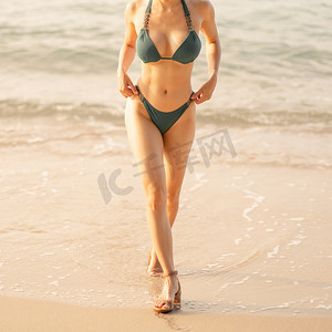 穿着绿色比基尼在海滩上行走的女人身体的特写。