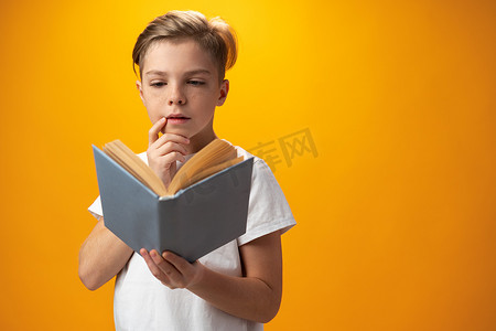 黄色背景下拿着一本书的小男学生