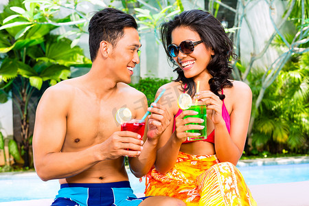 亚洲夫妇在泳池边喝鸡尾酒