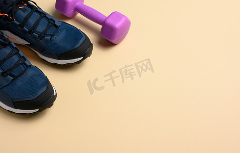 一双蓝色运动鞋和米色背景的紫色哑铃，运动。
