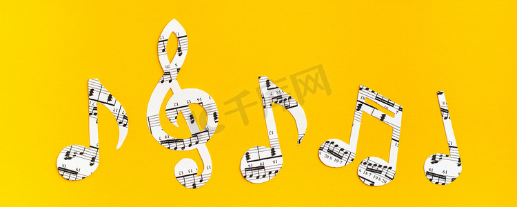 音乐创意音符摄影照片_音符和谱号从纸上剪下来，在黄色背景上连续排列音乐文本。