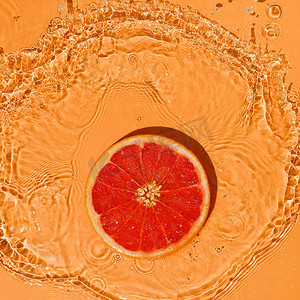 橘红泼墨摄影照片_夏季水果概念柑橘红葡萄柚在明亮的橙色背景上溅起水花。