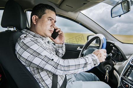 一名男司机在车里打电话，男子开车时打电话的概念，一名年轻人坐在车内使用手机的侧视图