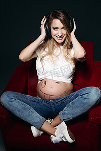 微笑的怀孕女性肚子上戴着大耳机。
