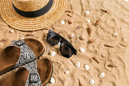 夏季沙滩装、人字拖、帽子、太阳镜和沙滩上的贝壳。