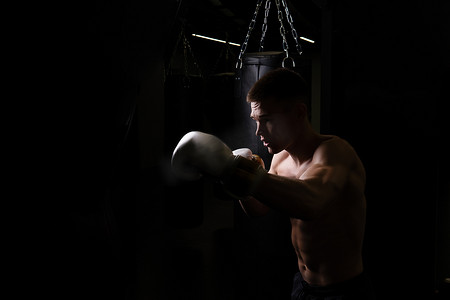 战士训练摄影照片_打击拳击手运动员练习袋手套黑色年轻职业拳击，为力量战士从战斗中锻炼生活方式，训练武术。