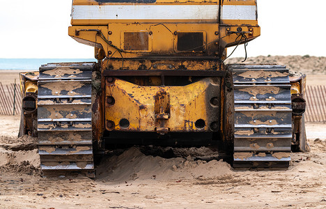 芝加哥海滩上一台旧大型工业黄色推土机背面的特写照片，其风化、磨损和生锈。