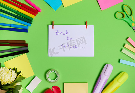 文具办公-无背景摄影照片_五颜六色的文具办公用品和学校配件排列成圆圈的顶视图，中间是白纸，上面写着“回到学校”。