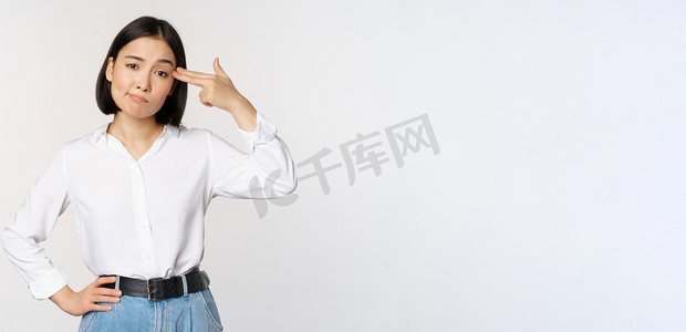 疲惫背景摄影照片_疲惫的亚洲女性的形象，对某些事情感到恼火，用手指指着她的头，站在白色背景上