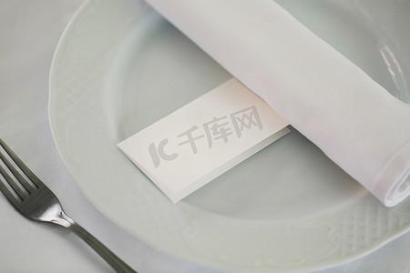 桌子上的盘子上有名字的卡片，上面有餐具，为餐厅的婚宴设置。