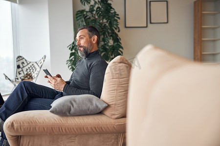 白人成年男子正坐在现代舒适的办公室休息区与智能手机