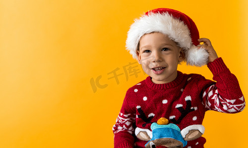 快乐微笑、积极、快乐、积极的学龄前小男孩的肖像，戴着红色温暖的圣诞老人帽子，在橙色、黄色背景上竖起大拇指。