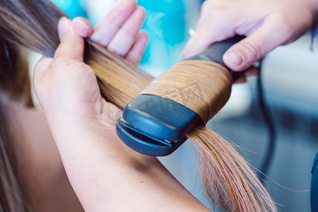 扁平女扁平摄影照片_理发师在女顾客的头发上使用扁铁