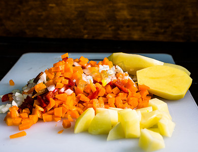 胡萝卜土豆摄影照片_新鲜和冷冻切碎的蔬菜、切碎的胡萝卜、土豆、洋葱和红甜椒在白色切板上。