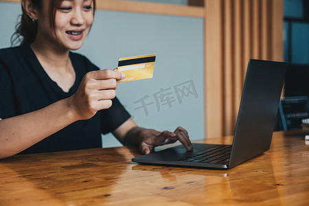 亚洲女孩持有银行信用卡并在笔记本电脑上打字、使用电脑在线购物、购买商品或在线订购、在网上银行报价中输入银行账户和详细信息的特写。