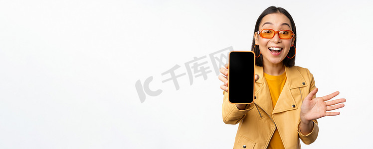 手机界面摄影照片_热情的亚洲女模特，在手机屏幕上展示智能手机应用程序界面、在线商店或网站，站在白色背景上