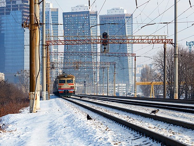 在阳光明媚的冬日，一列旧电动火车在摩天大楼城市景观的背景下在铁轨上行驶。