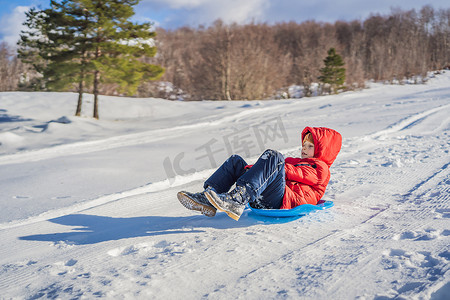 趣味画报摄影照片_快乐积极的小男孩享受雪橇和寒冷的户外天气，冬季趣味活动概念