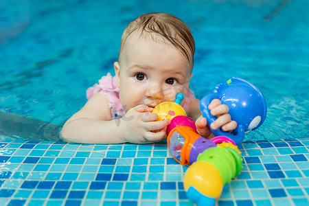 孩子游泳摄影照片_小女孩正在泳池里玩明亮的玩具