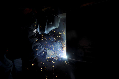 一名工人电焊工在半自动化工厂里烧钢。