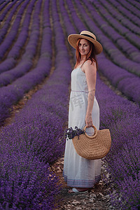 白色的裙子摄影照片_迷人的年轻女子，戴着帽子，穿着白色的裙子，在紫色的薰衣草田里。
