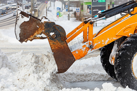 拖拉机在一个大金属桶的帮助下清除城市街道车道上的大量积雪。