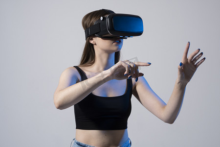年轻女子的特写镜头站在工作室里，戴着 VR 眼镜，在虚拟空间中用手滑动滚动缩放，同时与社交网络中的对象进行交互。