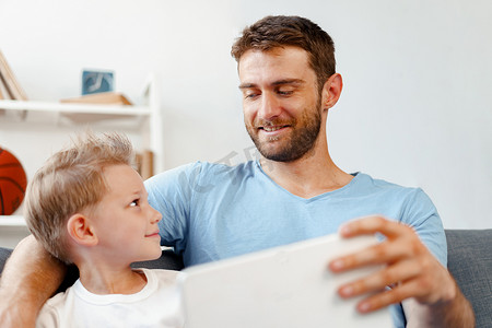 小男孩和他的爸爸一起坐在沙发上观看数字平板电脑上的视频