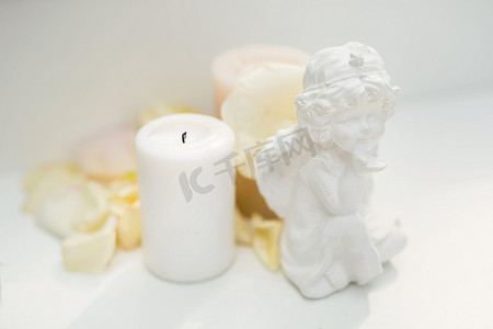 天使小雕像、蜡烛和桌上的玫瑰花瓣
