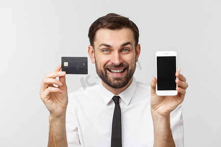 照片中，自信的企业家穿着西装，打着领带，手持智能手机和信用卡，在灰色背景下进行在线支付。