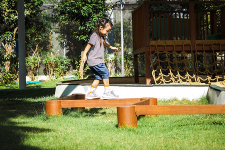 活跃的小女孩在公园的室外操场上平衡木行走。