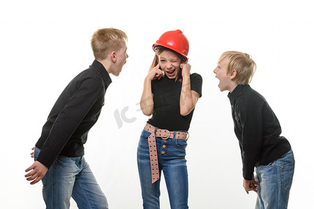 两个男孩对一个女孩大喊大叫，女孩戴着头盔站在头盔里堵住耳朵